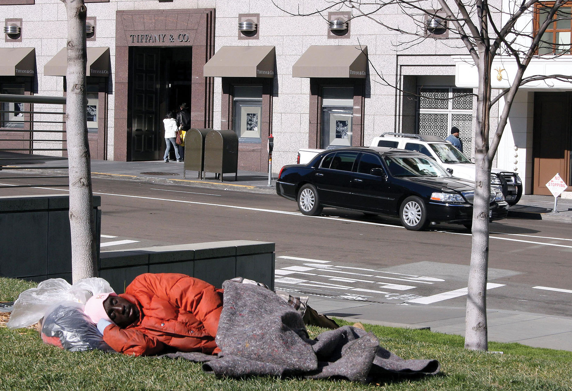 A homeless man sleeps on a bench just across the street from the luxurious Tiffany & Co jewelry store. in San Francisco. (Photo by Paula Steele.)