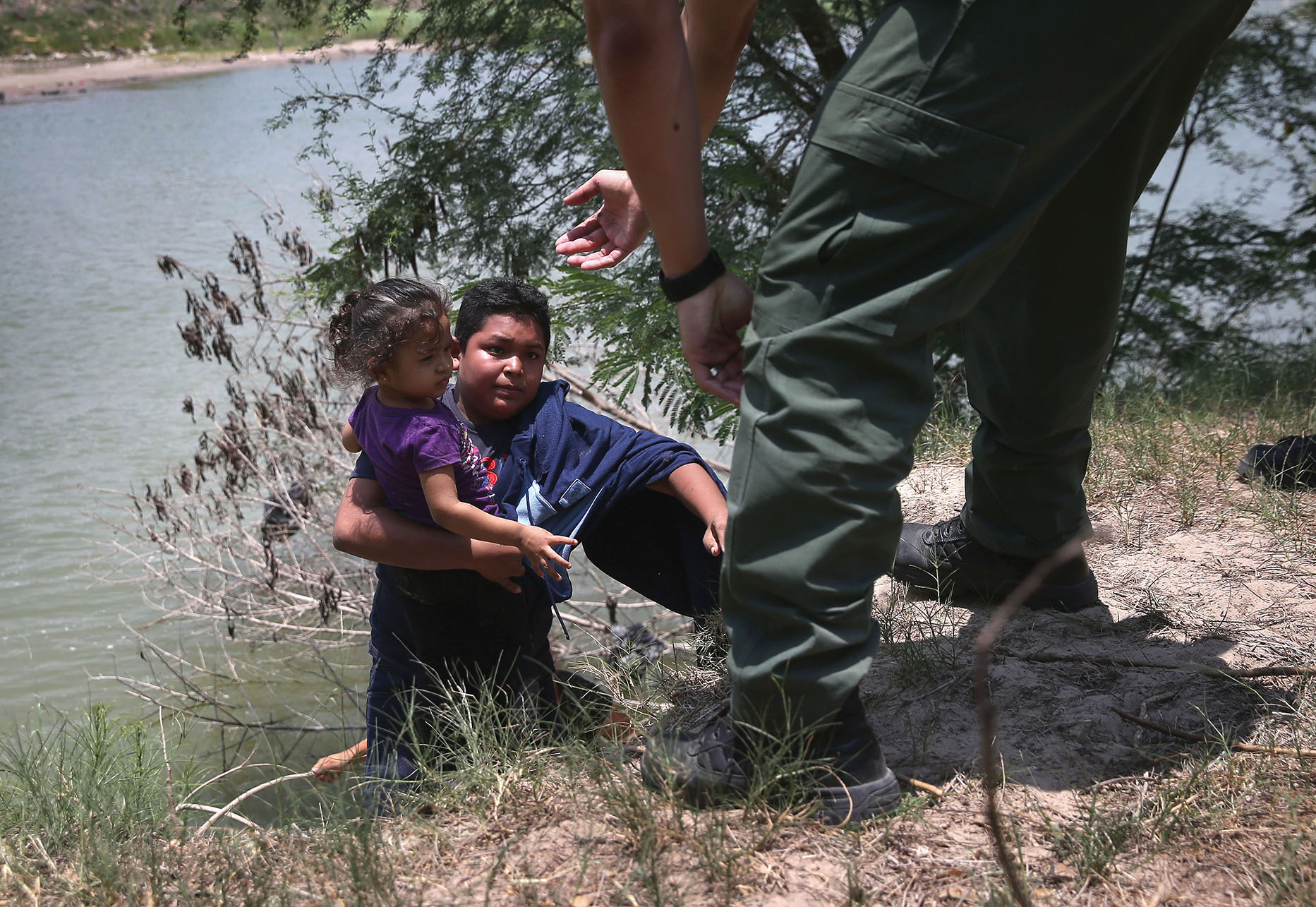 A U.S. Border Patrol agent assists undocumented minors up out of the water while crossing the Río Grande in July 2014. (Photo by John Moore/Getty Images.)