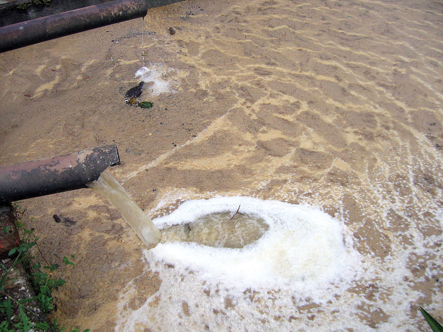 Contaminated water pours from a pipe into a brown, foaming pool in Nicaragua. (Photo by Ben Garland.)