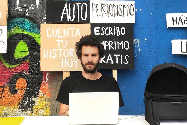 Dani Zelko, bearded in a black t-shirt, sitting behind a laptop computer.