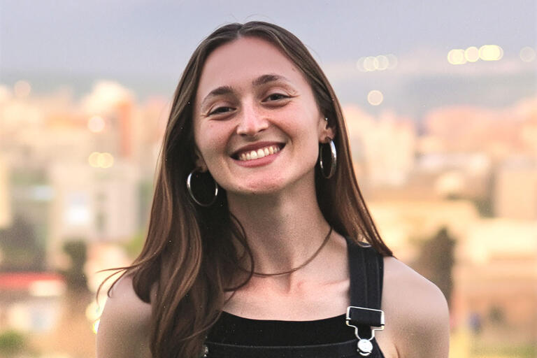 A portrait of Kate Cullen, a young woman with long dark hair wearing black overalls.