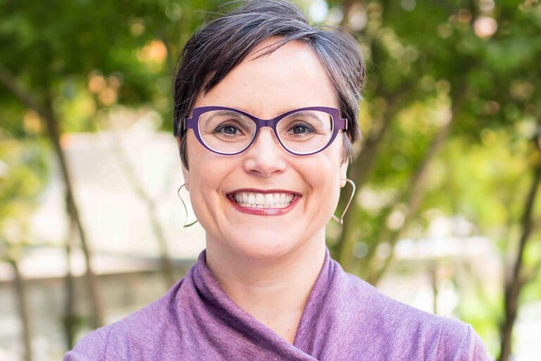 A woman with short hair gray-black hair in a purple shaw and purple glasses.