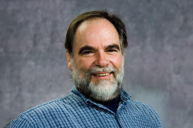 Middle-aged man with a gray and black beard and hair, posing in front of a gray background