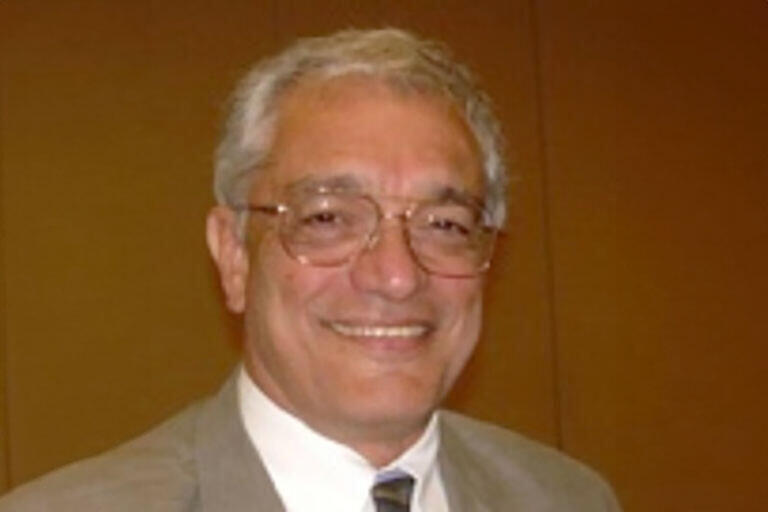 Picture of an older man with glasses, white hair, and a suit on with a brown background