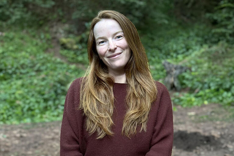 Woman with blonde hair, and a red sweater in a forest clearing