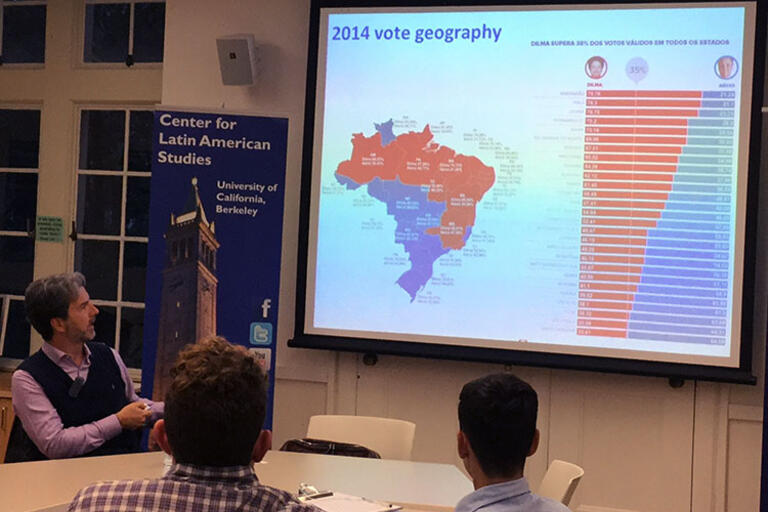 Carlos Milani seating down and showing a map of the regional divide in Brazilian voting