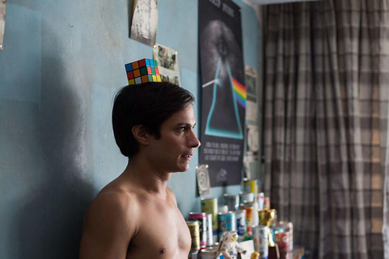 Gael García Bernal standing in front of a blue wall with a cube on top of his head
