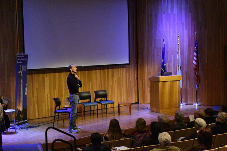 Charles Ferguson wearing a black sweater standing in front of the audience