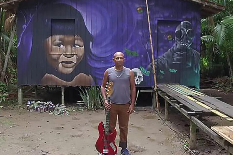 Man standing up with a guitar in front of a purple house 