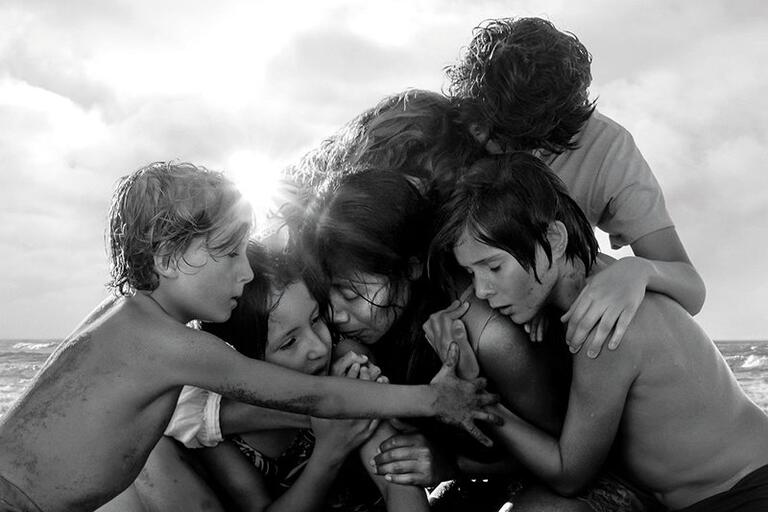 A group of children hug in a pile at the beach