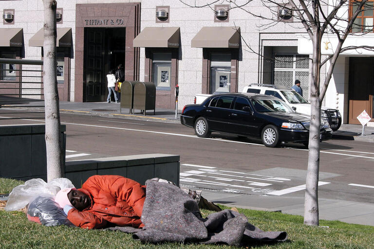 A homeless man sleeps on a bench just across the street from the luxurious Tiffany & Co jewelry store. in San Francisco. (Photo by Paula Steele.)