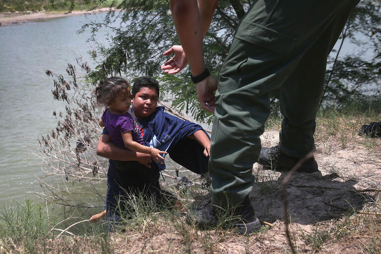 A U.S. Border Patrol agent assists undocumented minors up out of the water while crossing the Río Grande in July 2014. (Photo by John Moore/Getty Images.)