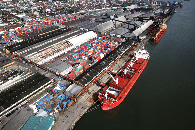 The busy port of Santos, Brazil, with ships being loaded by overhead cranes from a large storage facility for shipping containers.. (Photo courtesy of the Program for Accelerated Growth PAC.)