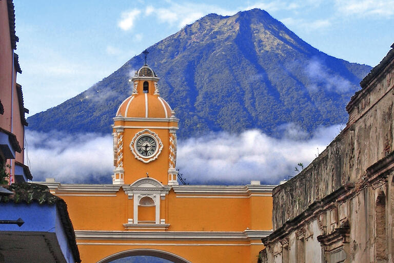 The orange Arch of Santa Catalina against a blue sky with the Agua Volcano looming in the background, Antigua, Guatemala. Photo by Dave Wilson.