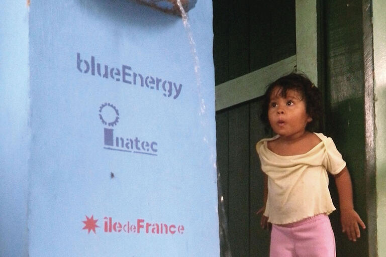 A young girl watches clean water pour out of a filtration unit in action. (Photo courtesy of blueEnergy.)