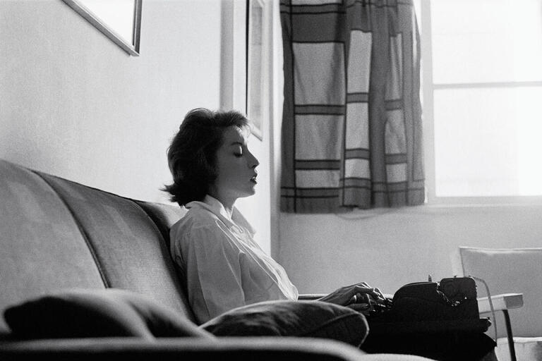 Clarice Lispector sits on a couch writing on a typewriter in 1961. (Photo by Claudia Andujar.)
