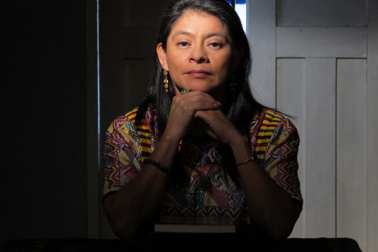 A woman stares intently at the camera with hands folded.