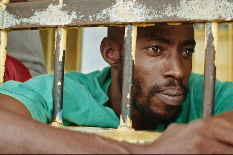Still from Carpinteros. A man looks through bars.