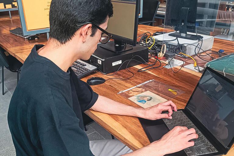 A student writes while sitting at a laptop.