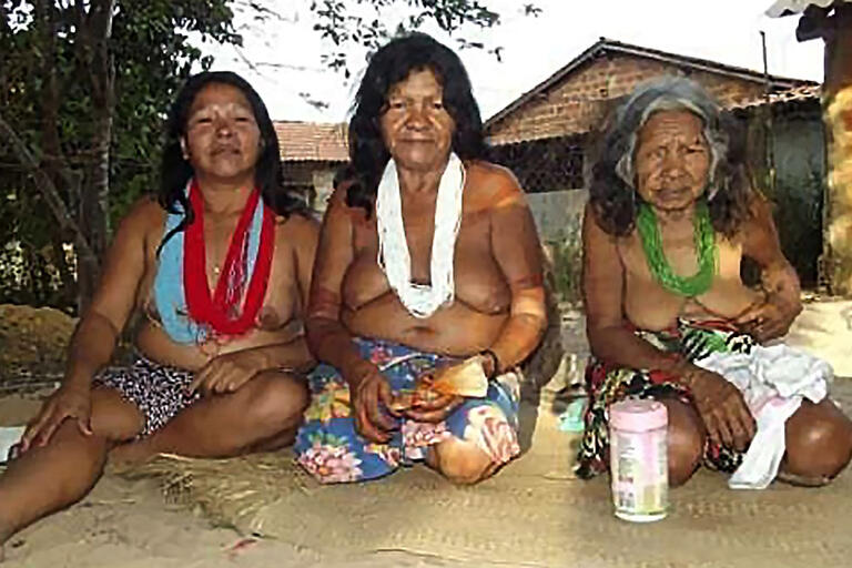 Three generations of Mehi women, in Indigenous garb, seated on the ground.