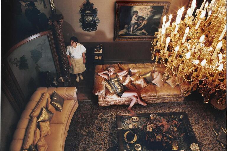 A woman lies on a couch in an opulent room while a maid stands by