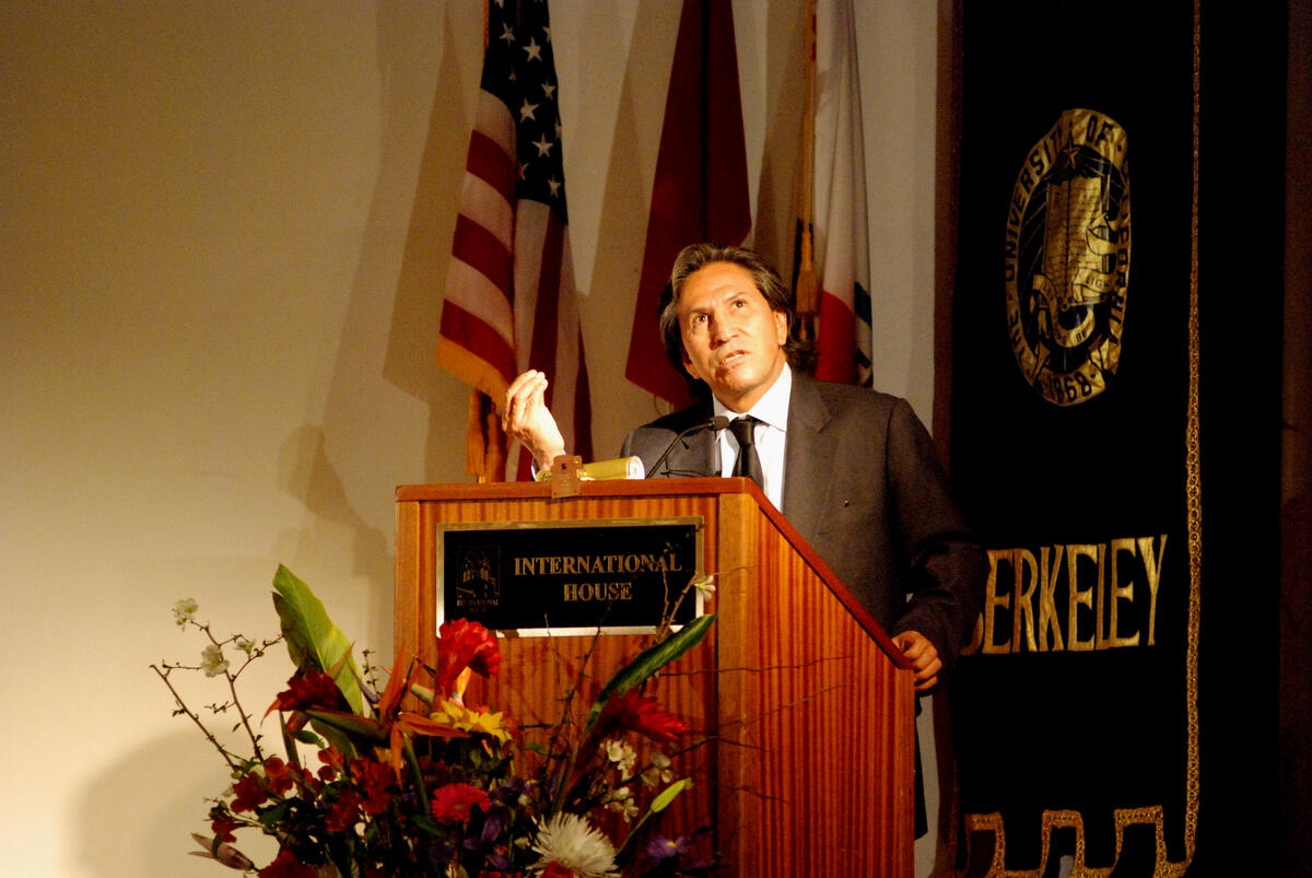 The speaker is projecting on a stage in front of a podium with hand gestures for emphasis.