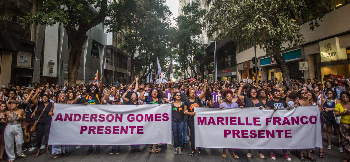 People marching with posters that read "Anderson Gomes Presente" and "Marielle Franco Presente"
