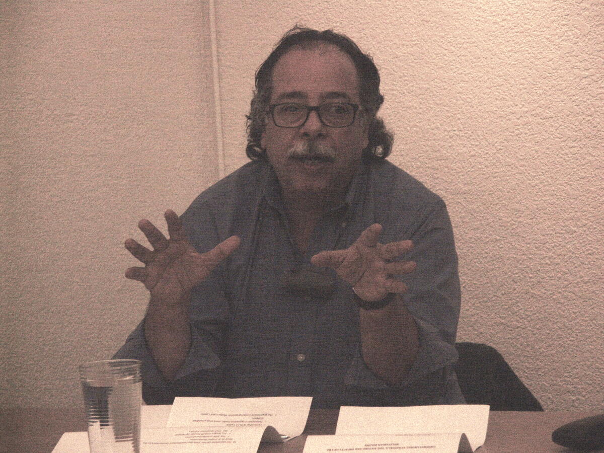 Alejandro Martínez Ubieda dicussing Venezuela’s recent electoral history The speaking is sitting at a desk, speaking to an audience while making hand gestures.