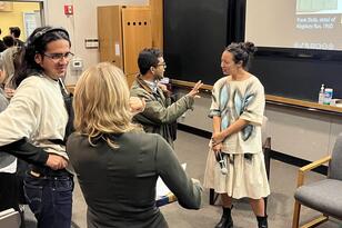 Students chatting after conversation. One students speaks to Irene Small at the front of the classroom.