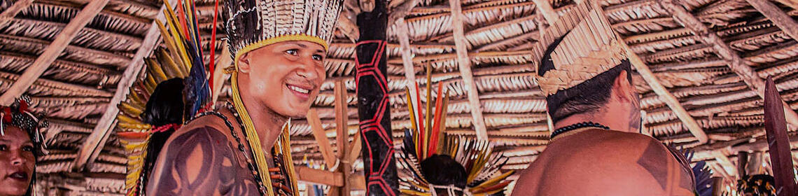 Indigenous people dance in a ceremony, wearing Indigenous headgear and body tattoos, carrying rattles.