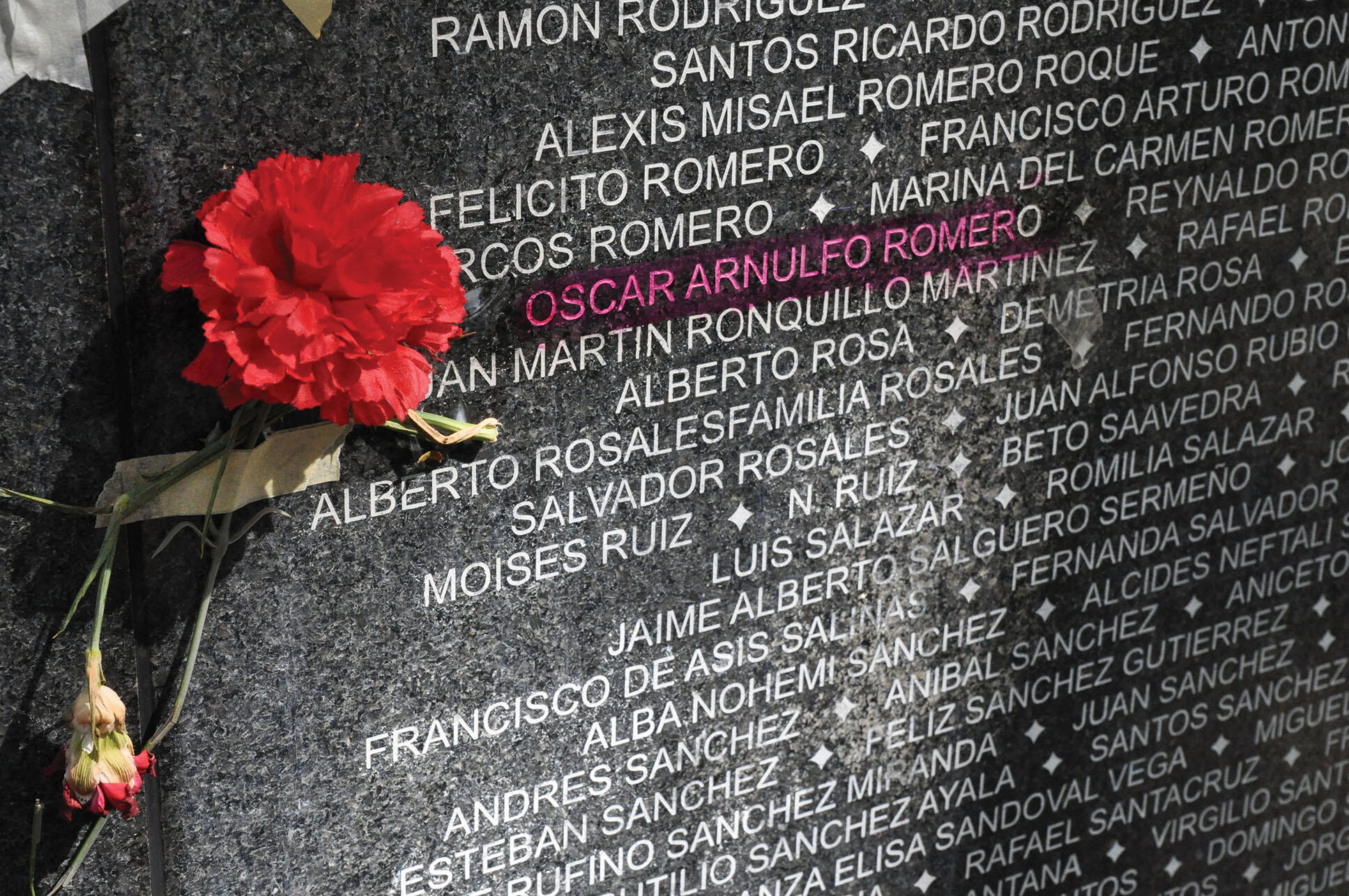 Archbishop Oscar Romero’s name highlighted on a black wall memorial listing the names of victims of violence in El Salvador. (Photo courtesy of the Archbishop Romero Trust.)