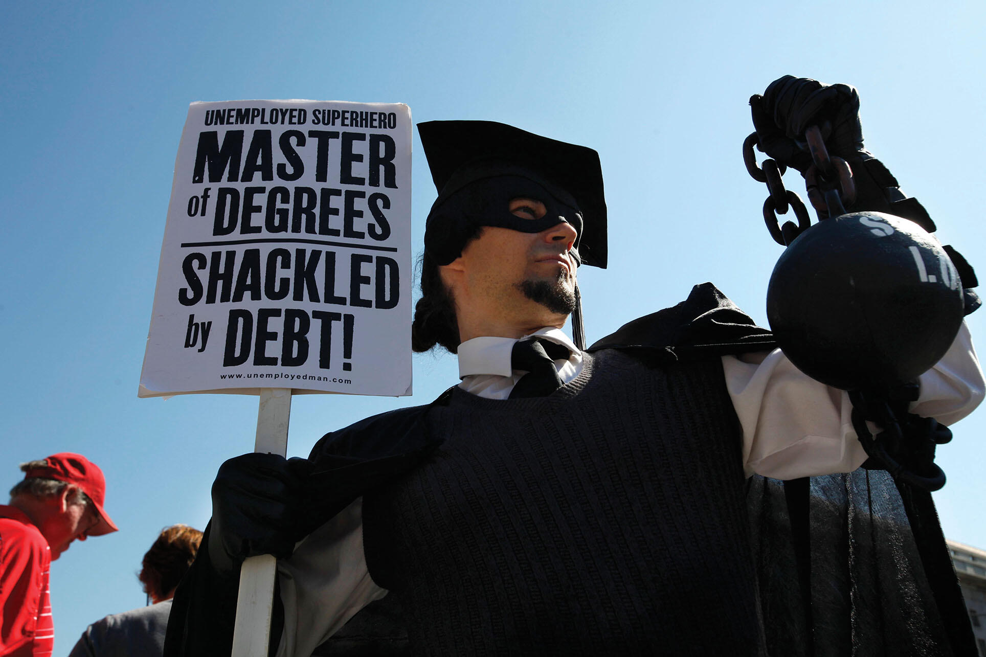 A protestor in the United States wears academic robes but holds a ball and chain symbolizing the burden of his educational debts. (Photo by Jacquelyn Martin/Associated Press.)