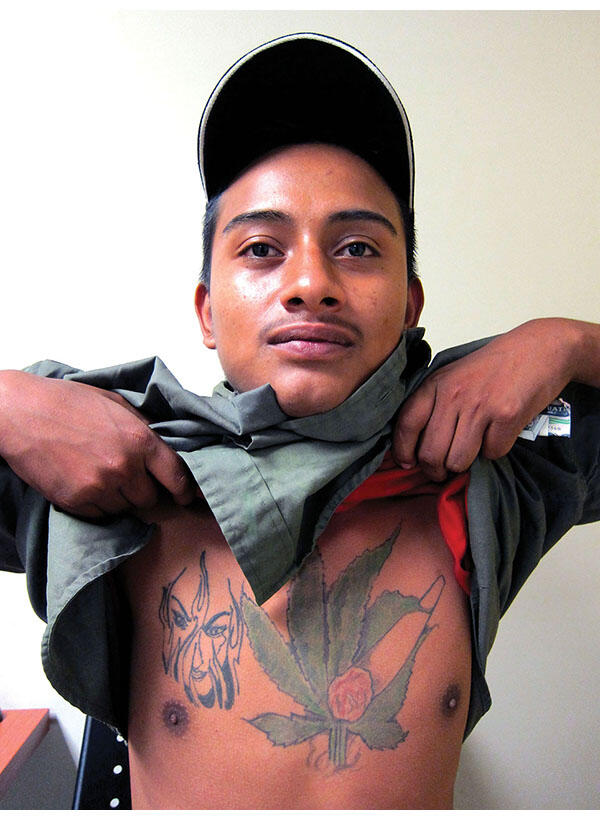 Andy, an informer against Guatemalan gangs, lifts his shirt and shows off his tattoos. (Photo by Anthony Fontes.)