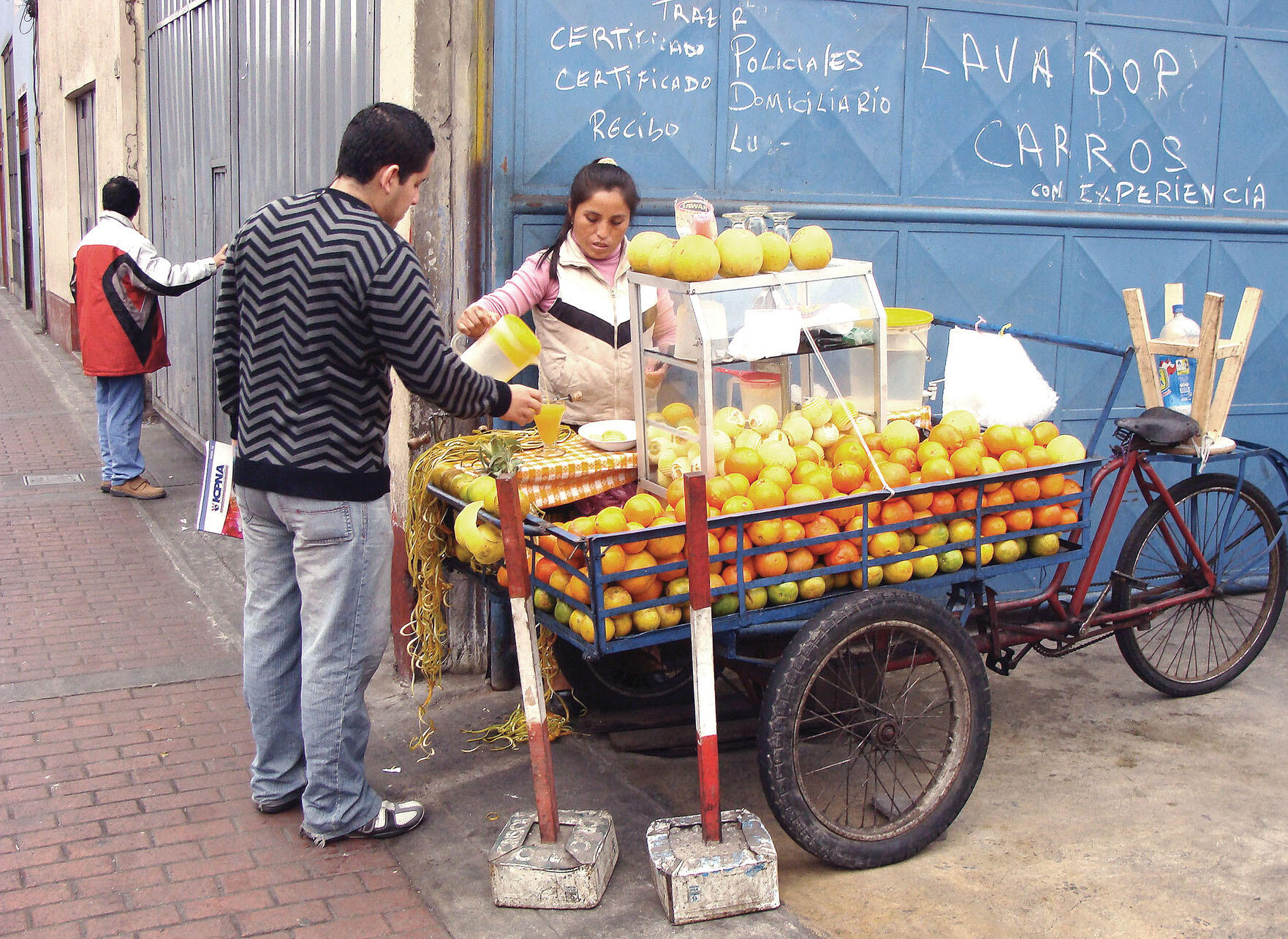 A fruit seller working from an old wooden handcart on the sidewalk makes a living in Peru’s informal labor market. (Photo by Julia Manzerova.)