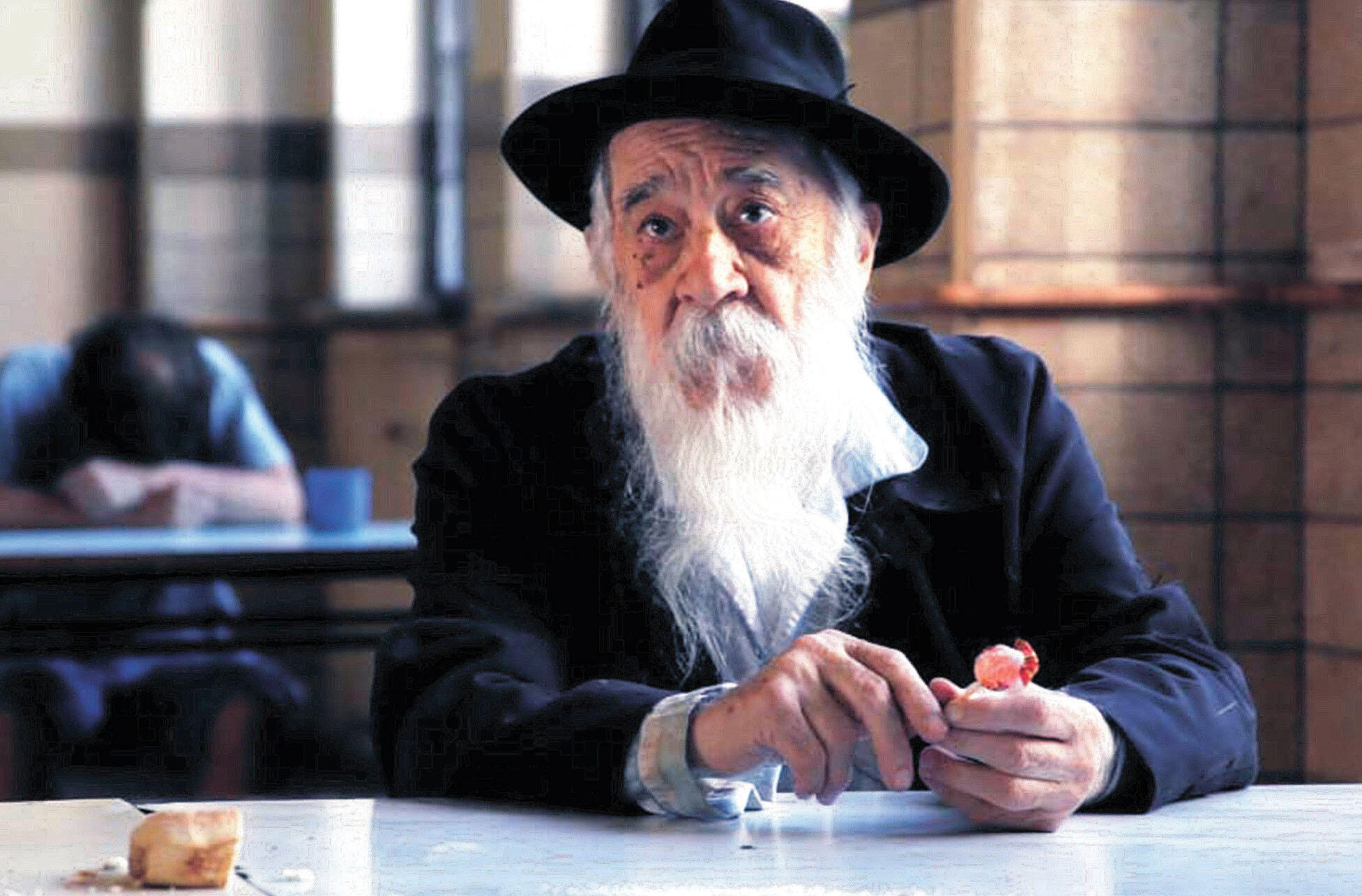 Fernando Birri as Remoro Barroso, sitting at a table in his trademark black hat and overcoat. (Photo courtesy of Orgon Films.)