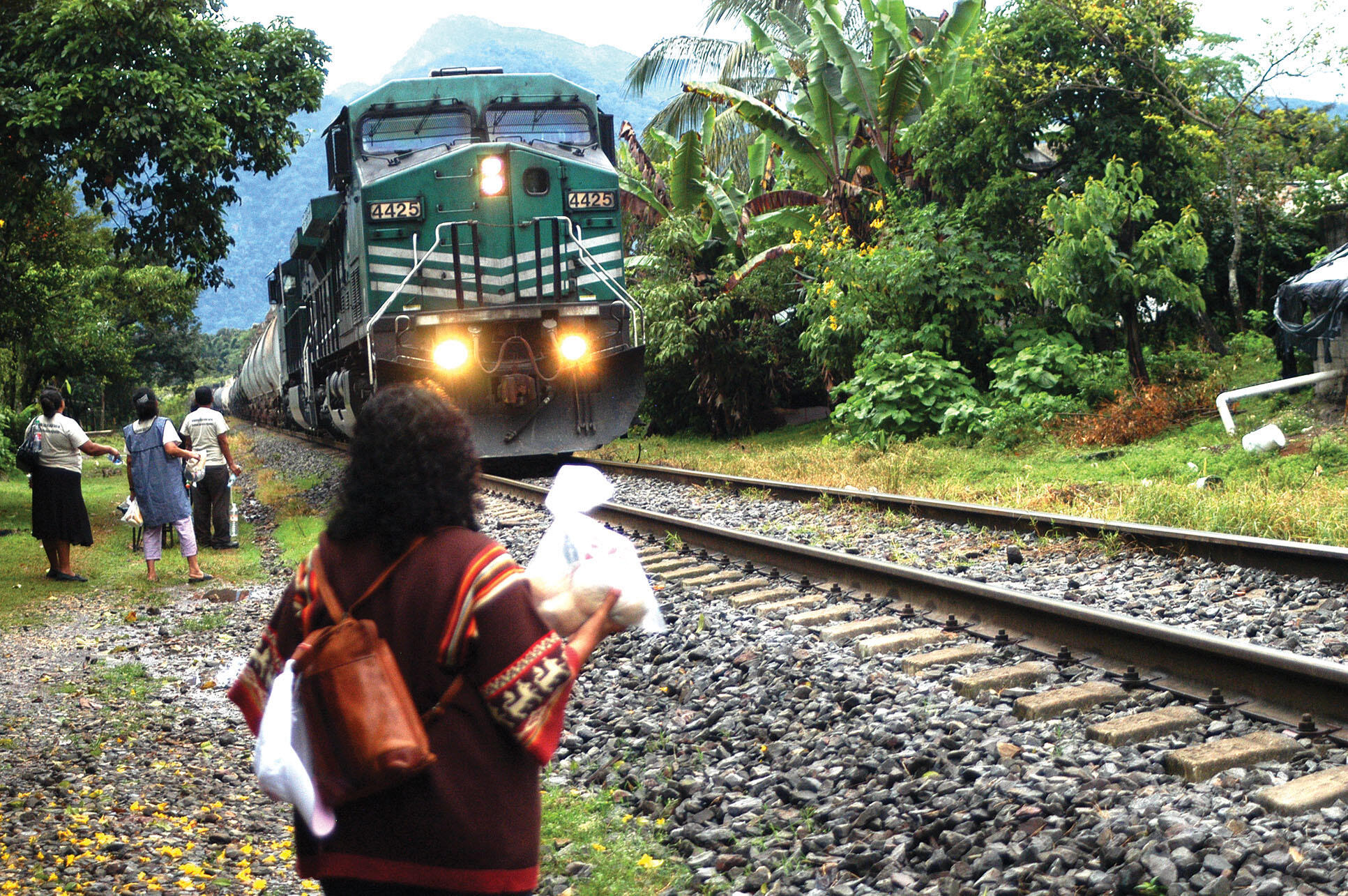 Women stand ready to throw food and water to the migrants riding atop the train as it passes through their town. (Photo by Mittchel C. Alcántara.)