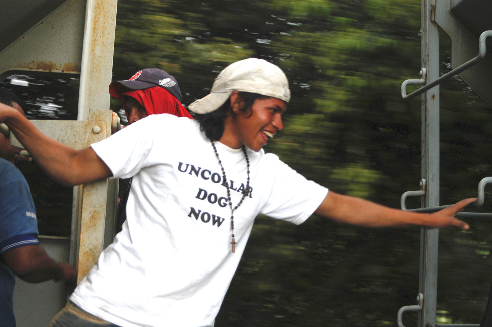 A young migrant reaches across the gape for a ladder on the next freight car aboard a moving train. (Photo by Mittchel C. Alcántara.)