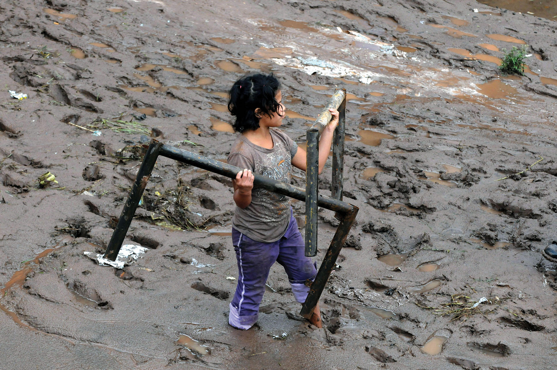 A young girl hauls away family possessions though deep mud after a flood in Honduras. (Photo by Globovision.)