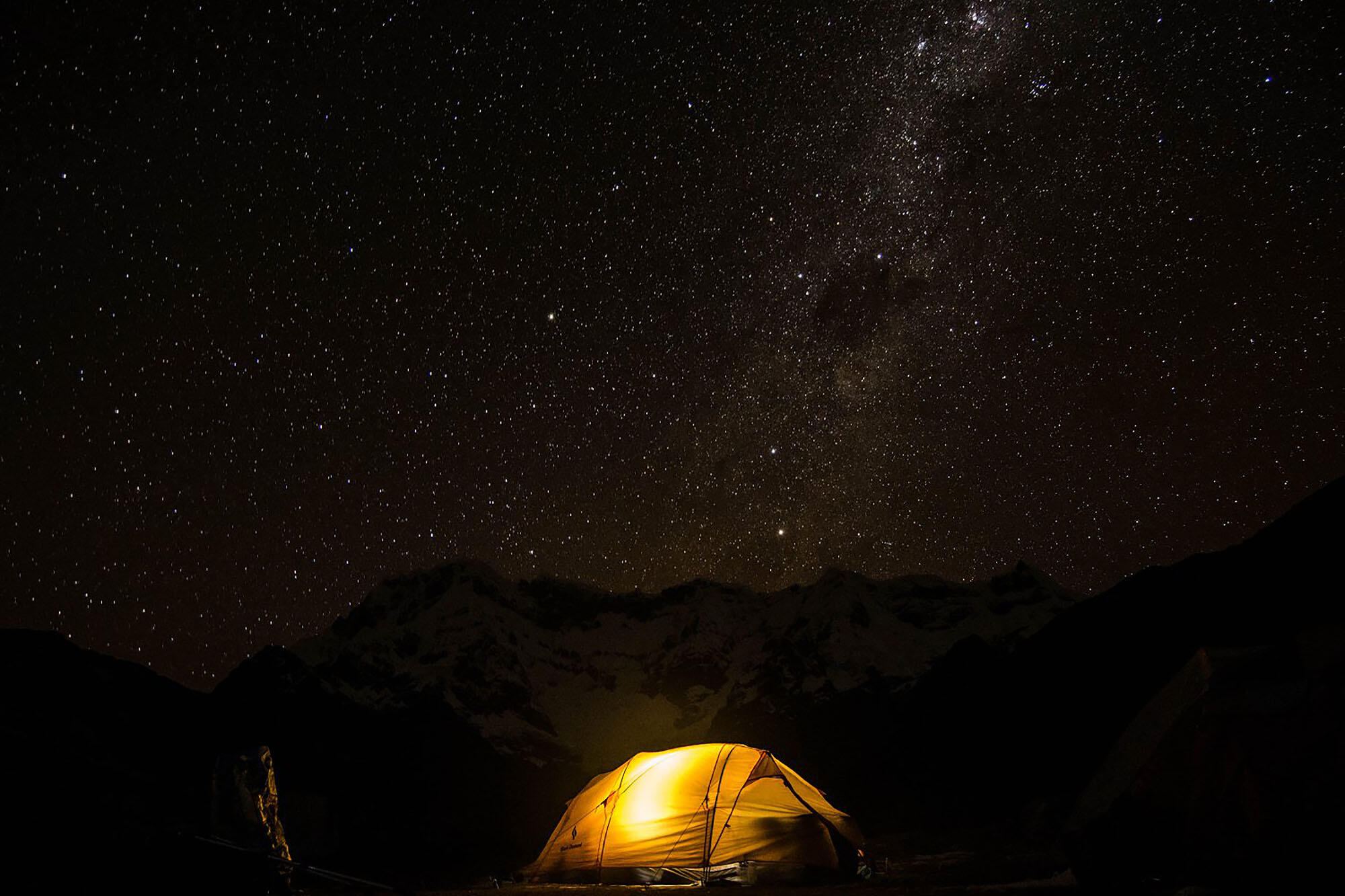 Photo of an illuminated tent under the stars; one of the many camps of the research team, at Upispampa. (Photo by Emma Steigerwald.)