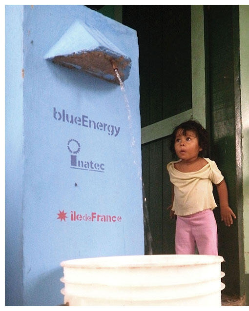  A young girl watches water pour from a filtration unit in action. (Photo courtesy of blueEnergy.)