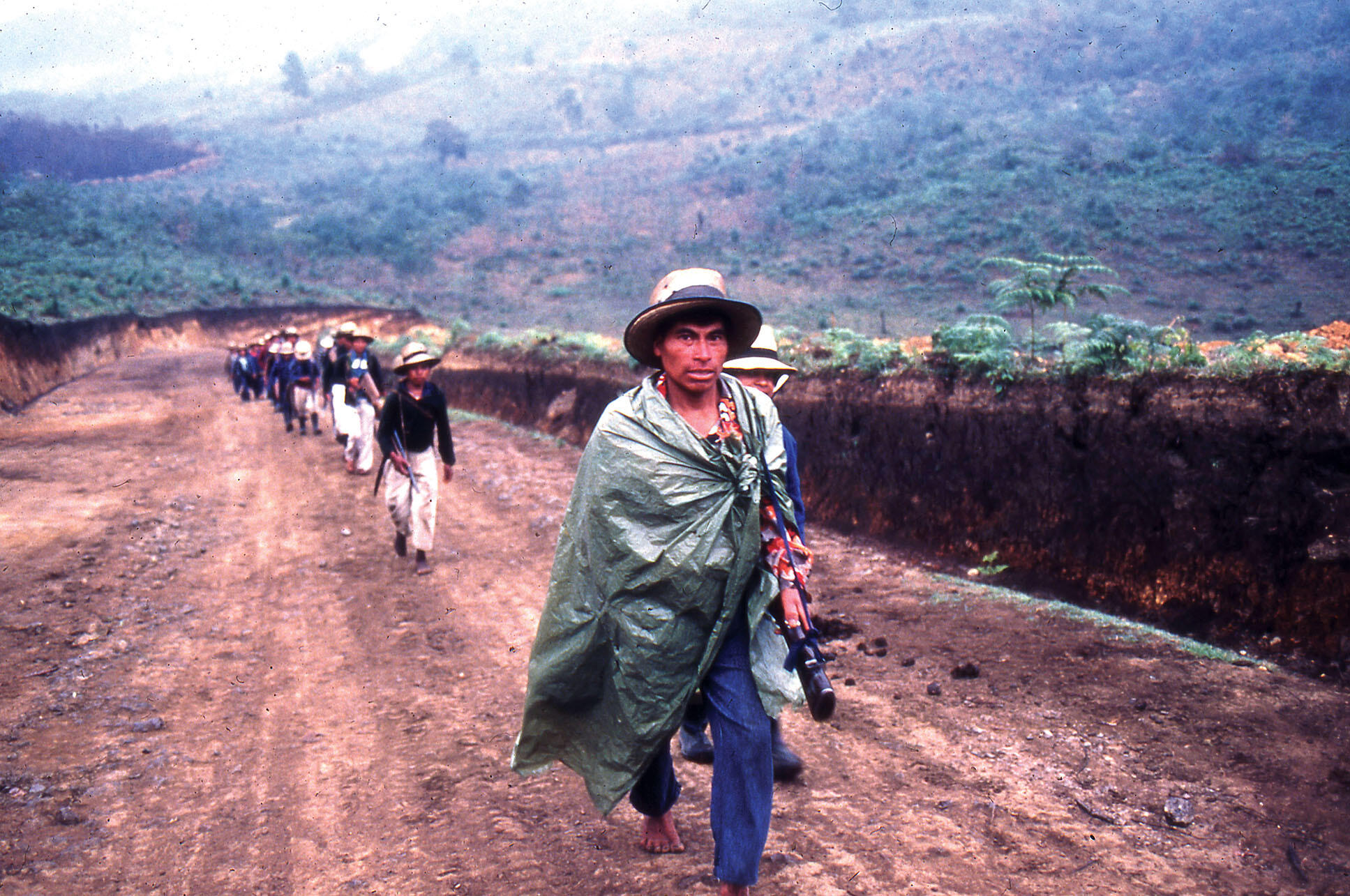 Barefoot men with assault rifles march along a road as part of a civil patrol (Patrullas de Autodefensa Civil, PAC), Ixil region, Guatemala, March 1983. (Photo courtesy of Beatriz Manz.)