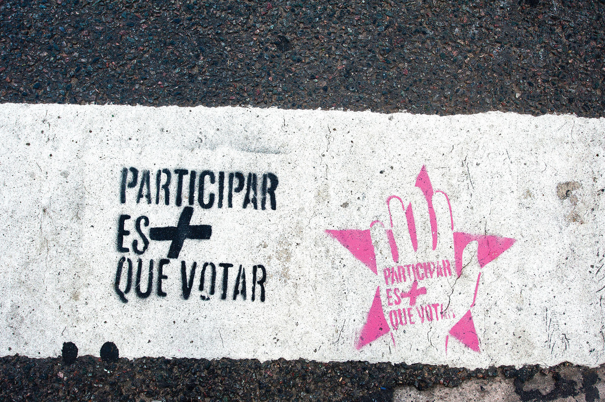 Graffiti painted on a sidewalk reads "Participation is more than voting." (Photo by Caitlin Margaret Kelly.)